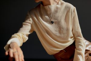 Close-Up Shot of a Person Wearing Beige Long Sleeves and elegant necklace