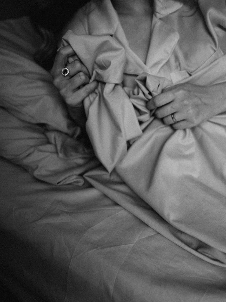 black and white close-up of a person clutching soft fabric, with visible rings on their fingers, creating a sense of comfort 