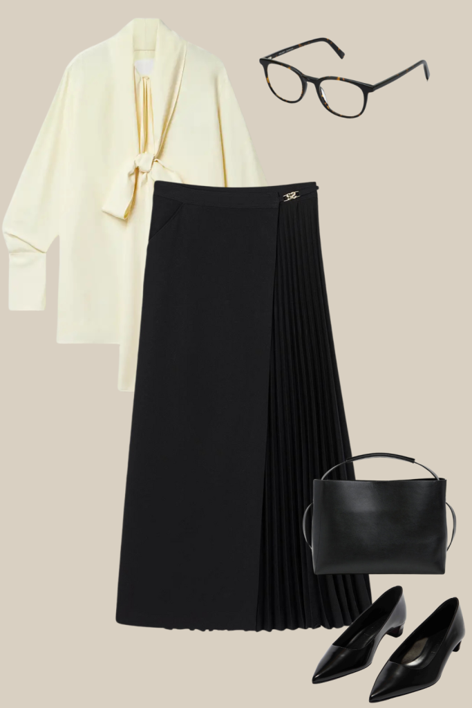 Chic Thanksgiving outfit idea featuring a cream tie-neck blouse, black pleated midi skirt, black structured handbag, classic black glasses, and black kitten-heel pumps. A refined, intellectual look perfect for a polished holiday celebration.
