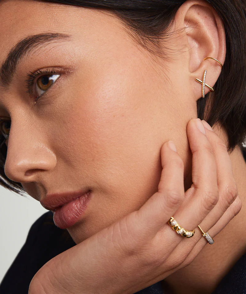 Close-up of a woman wearing stacked gold hoop earrings and diamond-studded rings, highlighting elegant, minimalist jewelry details.