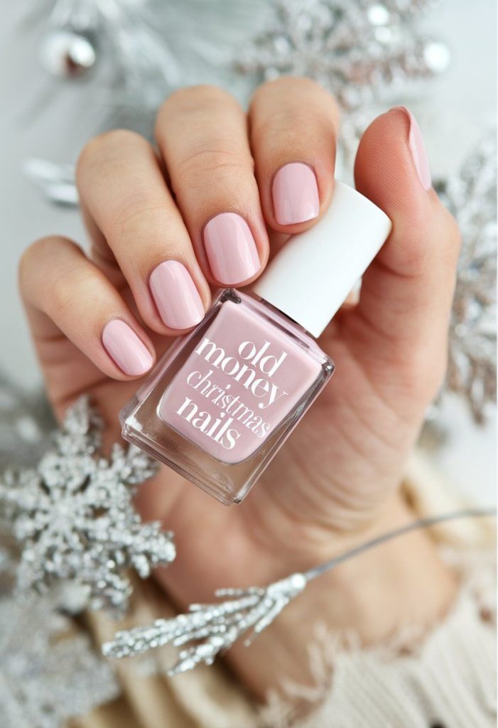 Elegant hand with manicured light pink nails, holding a bottle labeled "old money Christmas nails." The soft pink shade exudes a timeless, classic holiday style, with a refined and minimalist aesthetic.