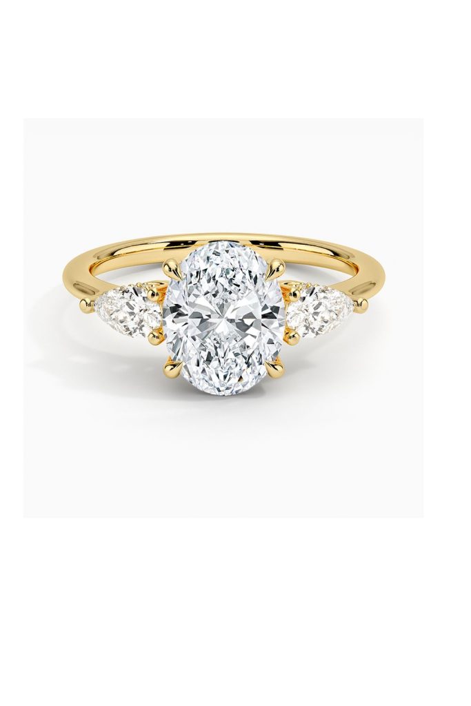 Oval-cut diamond engagement ring with pear-shaped side stones set in yellow gold, combining vintage charm with modern elegance.