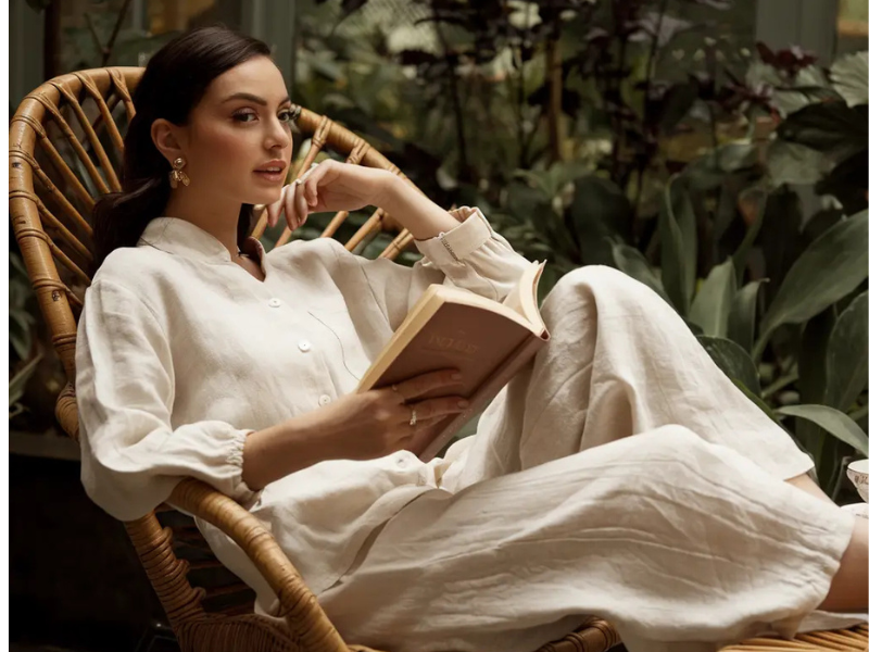 Woman in a cream linen outfit reading a book in a rattan chair, - a calm moment reflecting the elegance of an old money style blog.