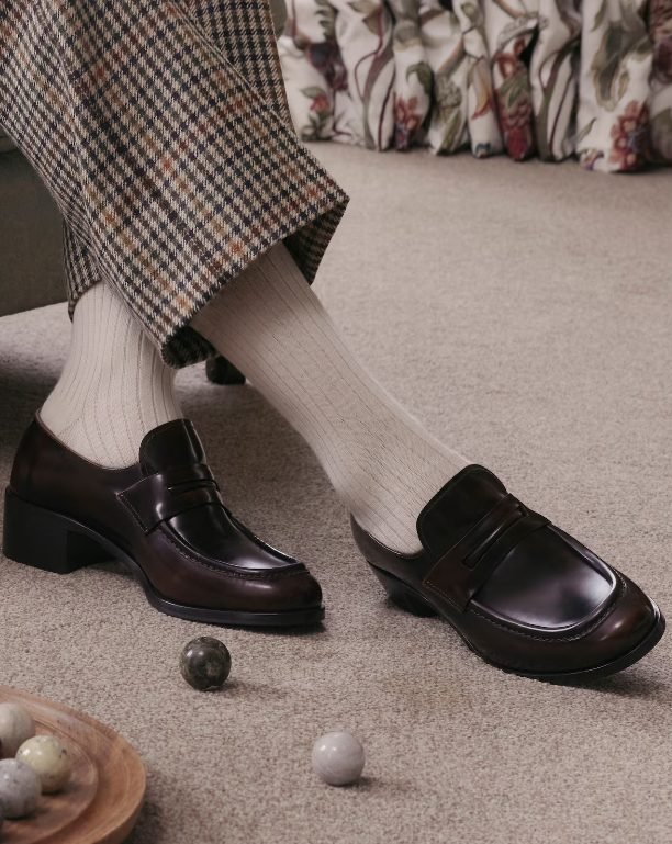 Dark leather loafers worn with socks and tailored trousers, relaxed yet refined old money shoe brands look