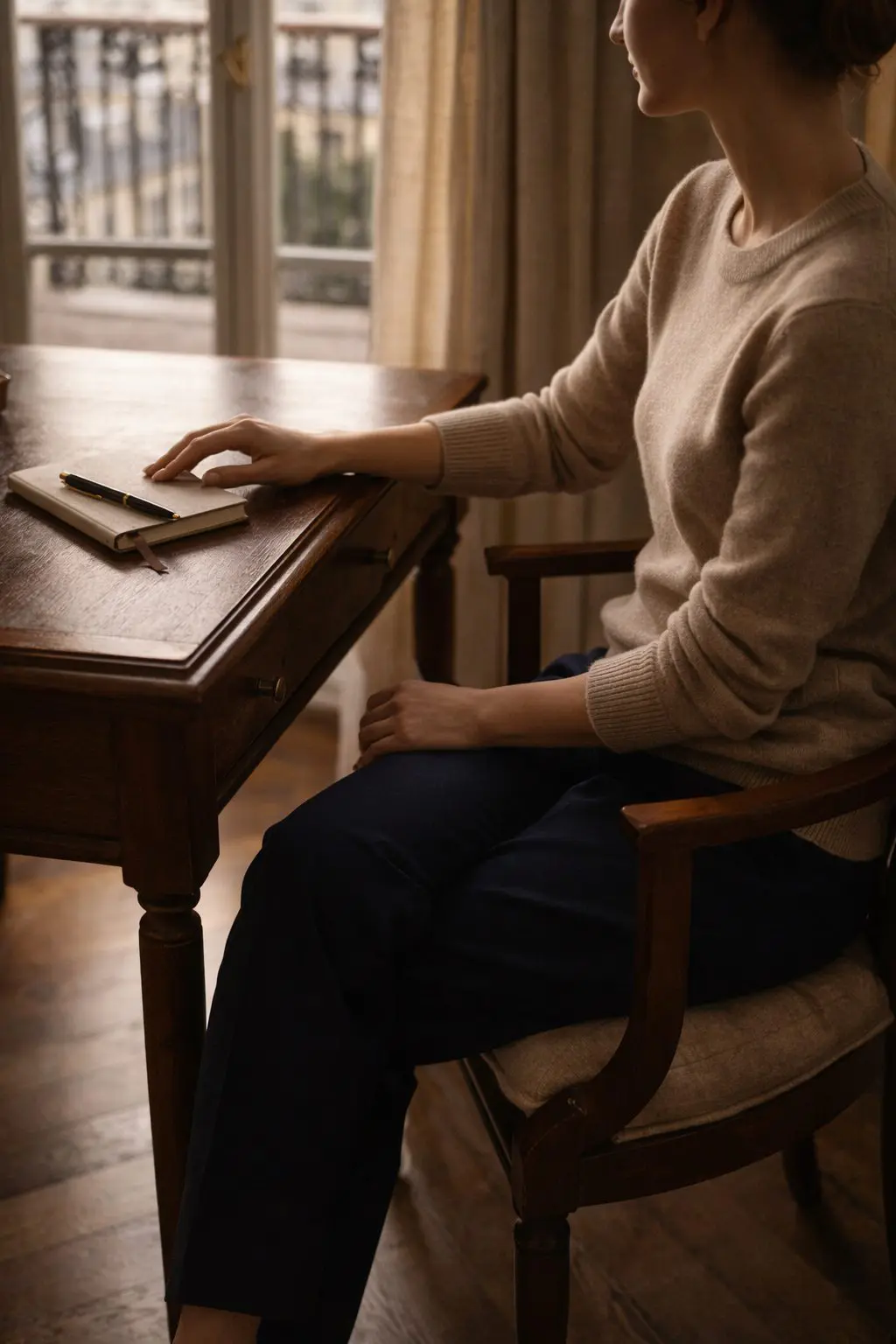 Woman seated quietly at a desk near a window, unobserved and calm, embodying Old Money Habits to Start in 2026.