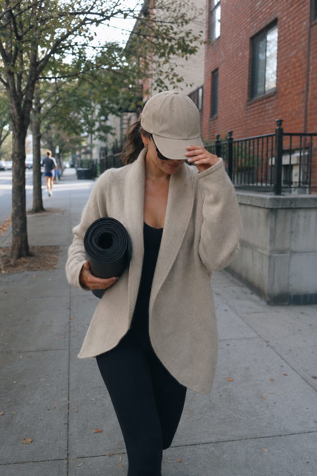 carolyn bessette style outfit: oatmeal oversized cashmere cardigan, black leggings, and a khaki baseball cap for an off-duty look