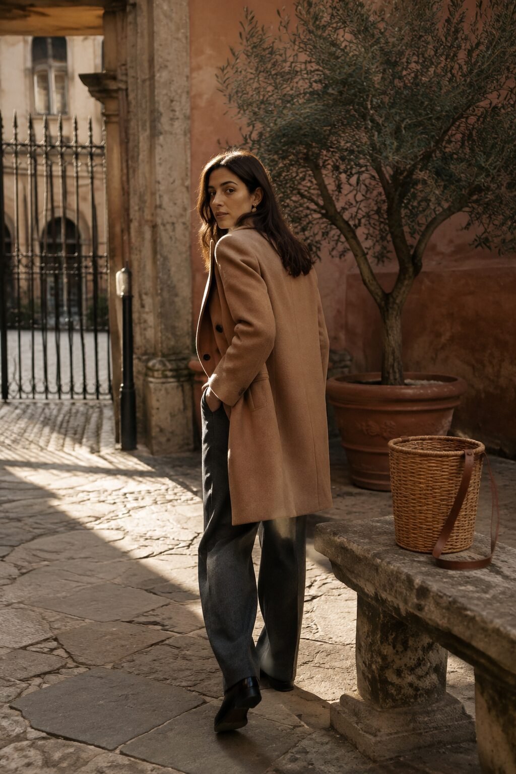 Woman in a camel coat and tailored trousers walking through an Italian courtyard
