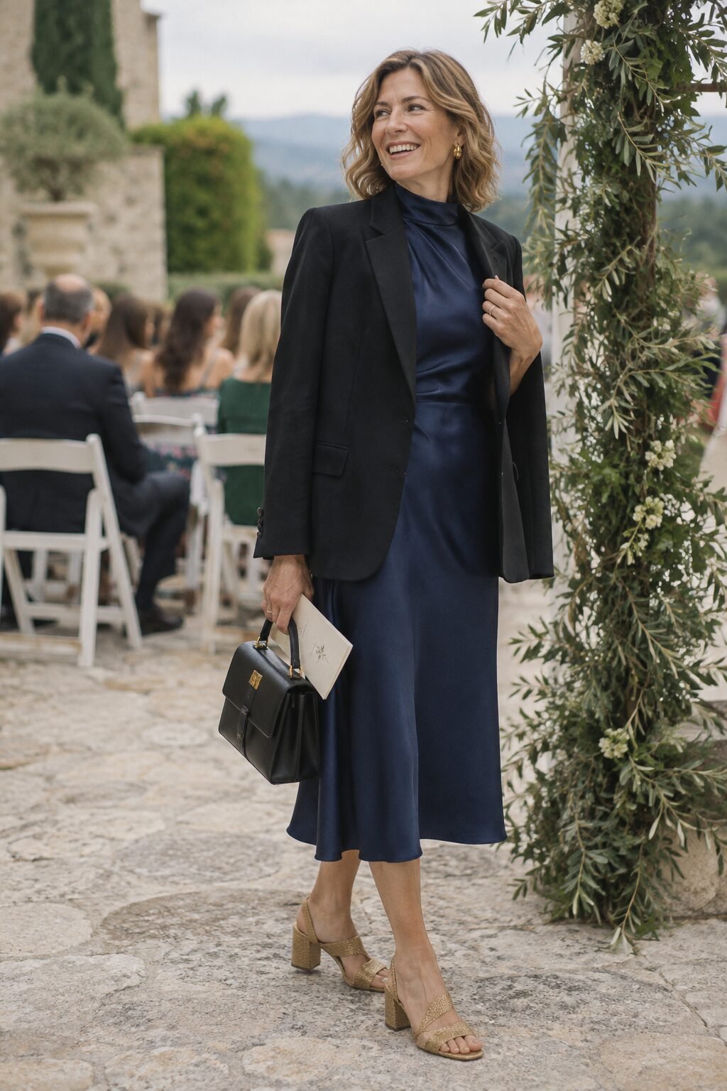 mother of the bride ceremony outfit: navy silk midi dress layered under a black blazer with gold block-heel sandals