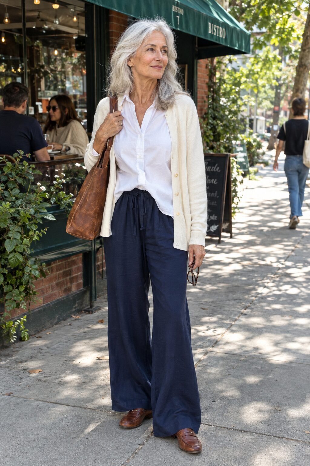 capsule wardrobe for women in their 70s: navy silk wide-leg pants, white poplin shirt, ivory cashmere cardigan and brown loafers for a lunch out