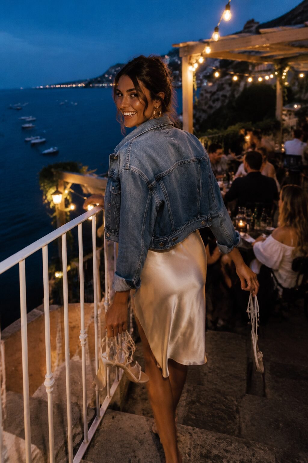 woman wearing a cropped denim jacket unbuttoned over a champagne silk slip dress for an elegant date night outfit