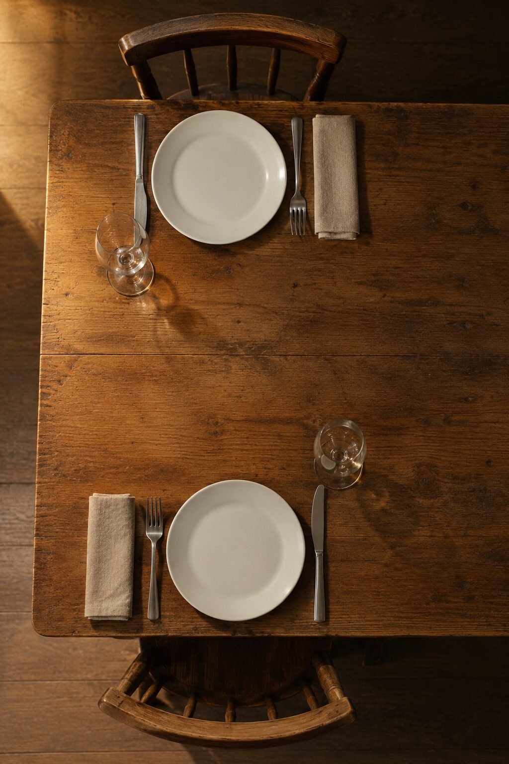 romantic table setting for two with place settings arranged corner to corner at one end of a wooden dining table