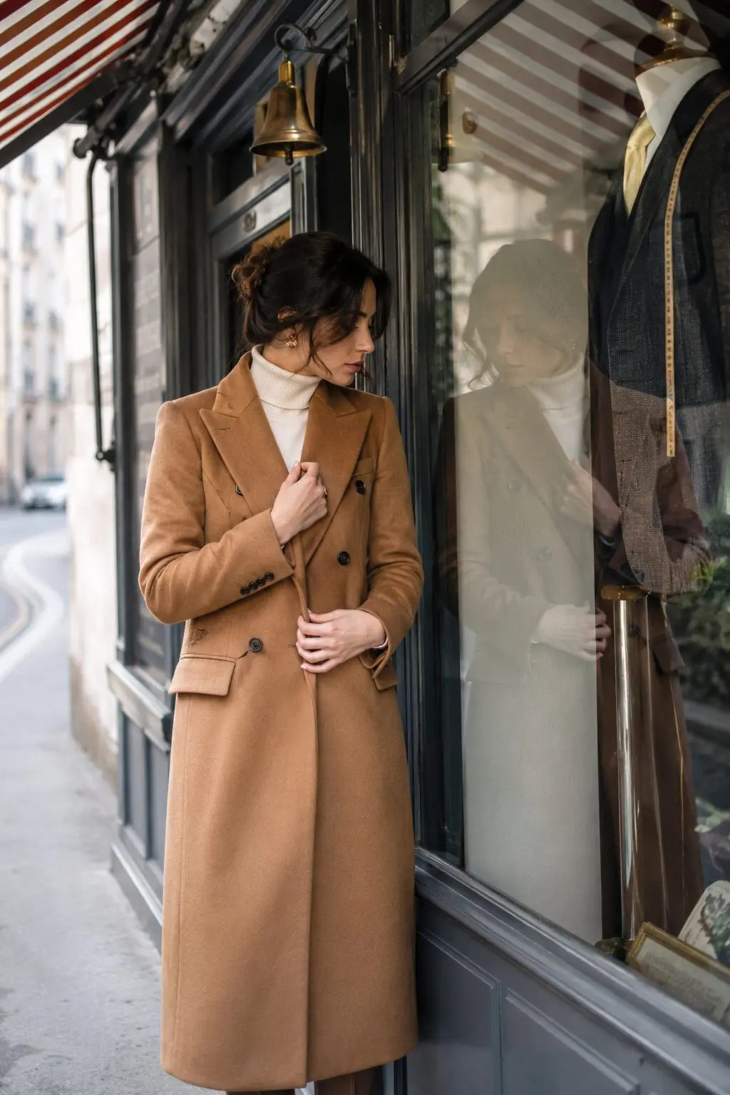 camel wool coat worn buttoned outside a boutique shop window