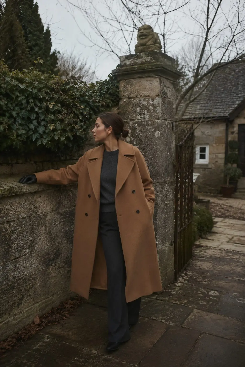 camel wool coat worn open over a charcoal knit at a stone garden gate