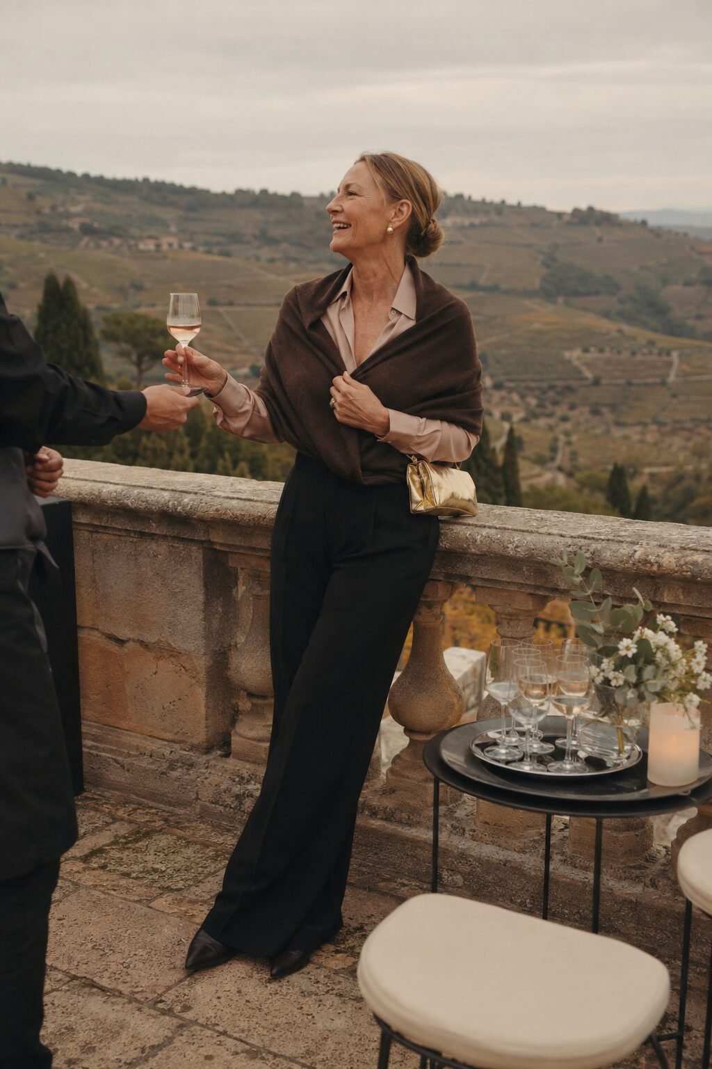 mother of the groom cocktail hour outfit: black trouser, blush satin top, brown cashmere wrap, and gold clutch