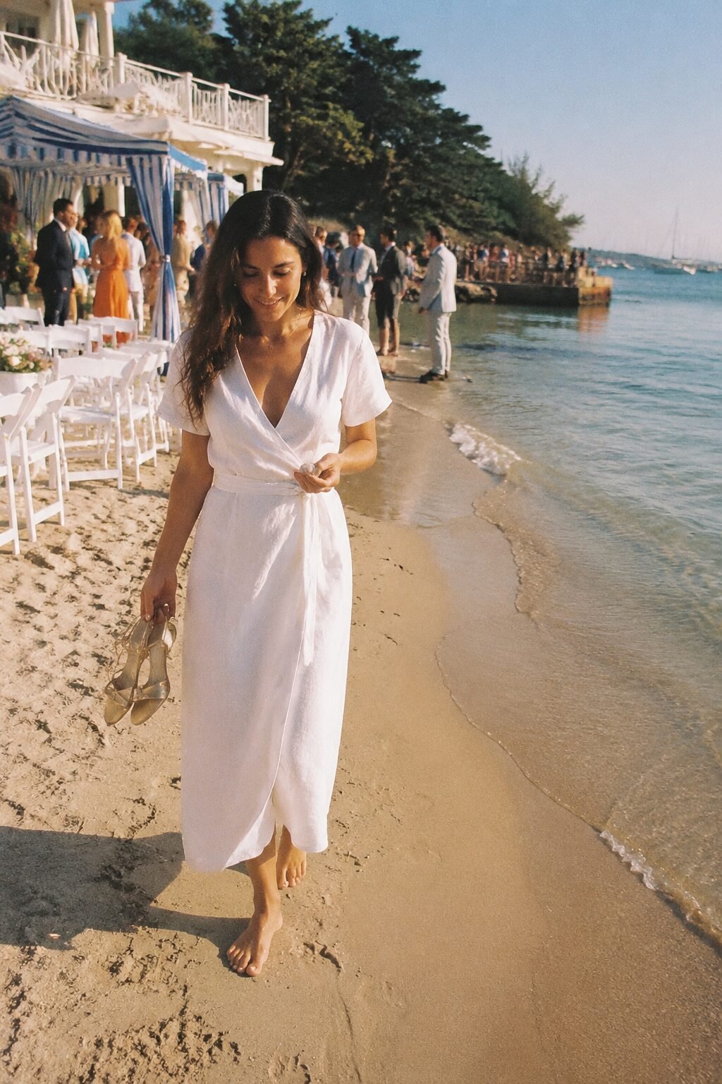 old money wedding guest dress: white linen wrap dress with gold strappy sandals for a destination beach wedding