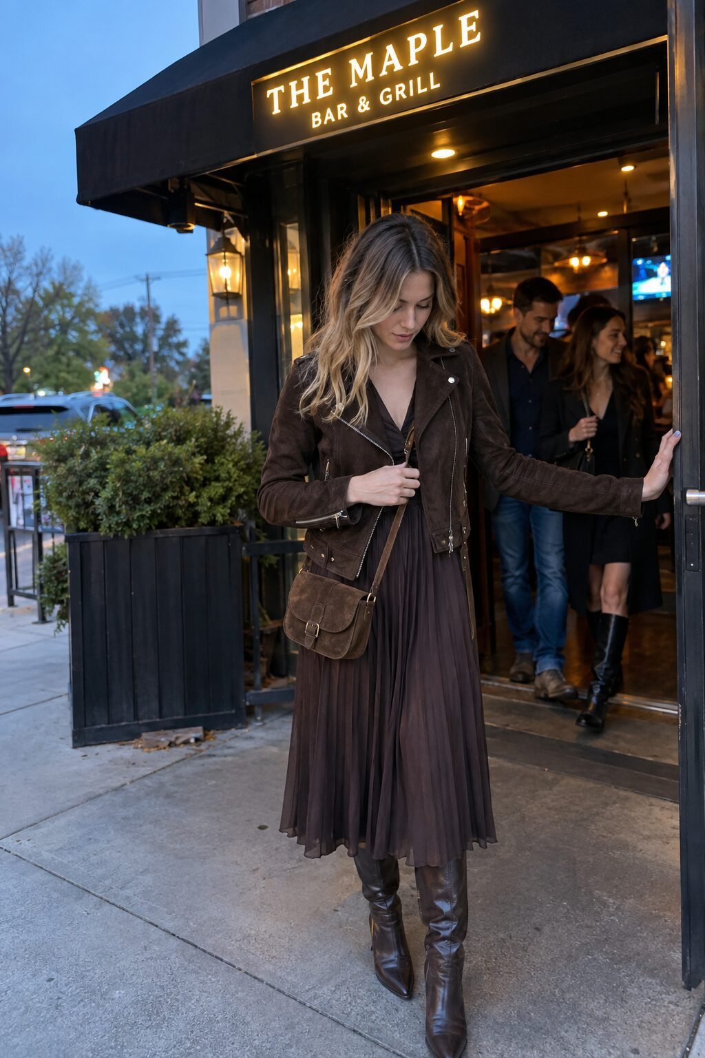 elegant post-tailgate outfit: chocolate suede moto jacket, dark brown pleated midi skirt, and chocolate knee-high boots