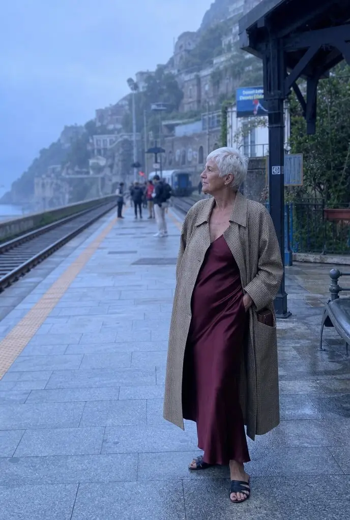 fall travel outfit for women in their 70s: mahogany silk slip dress under a belted khaki trench coat