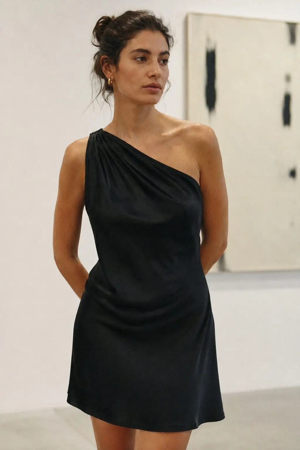 black charmeuse one-shoulder slip dress with draped asymmetry, worn alone for an art gallery opening