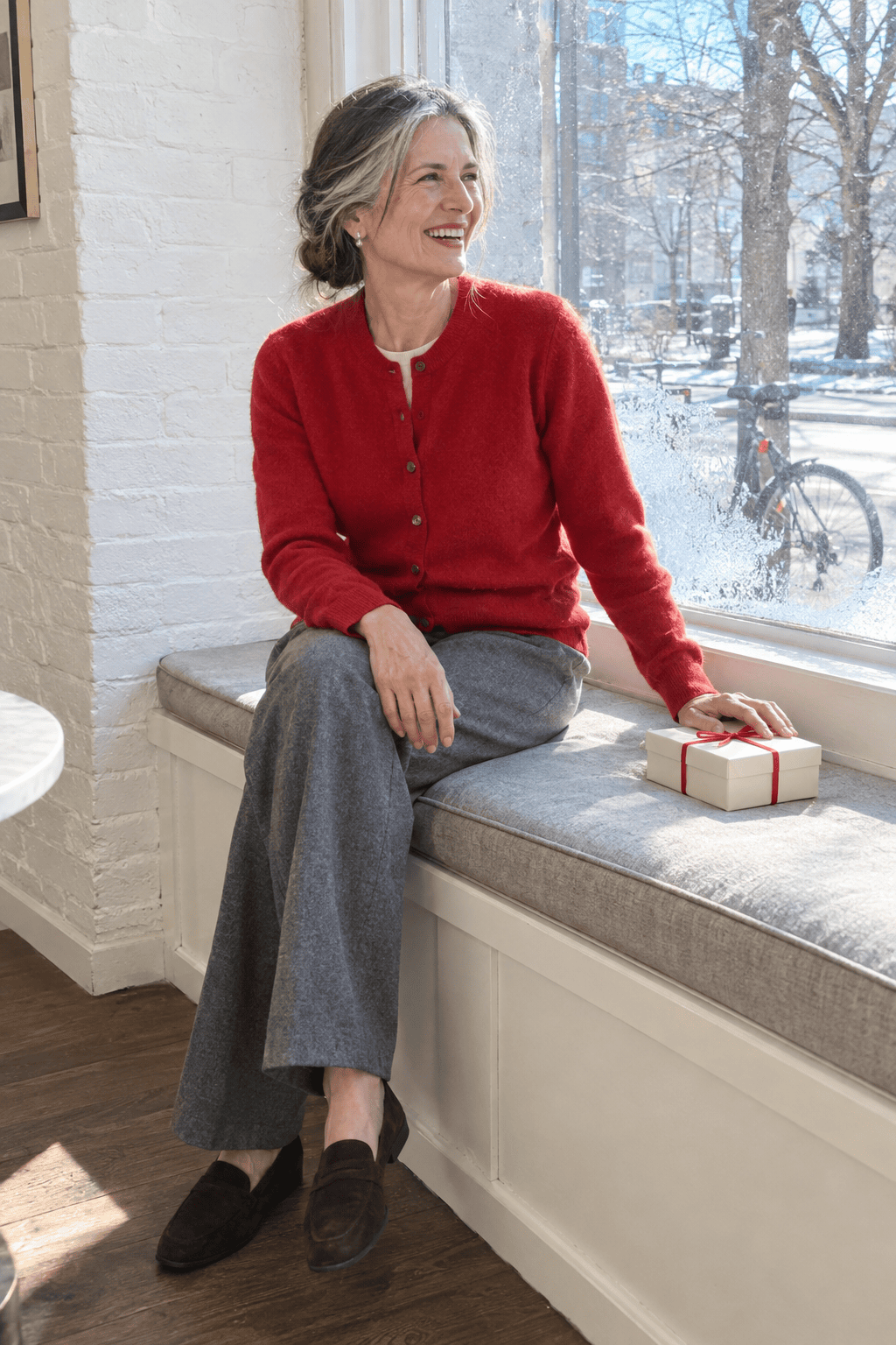 Galentine's lunch outfit for women over 60: poppy red cashmere cardigan buttoned over an ivory silk shell with grey flannel trousers and suede loafers