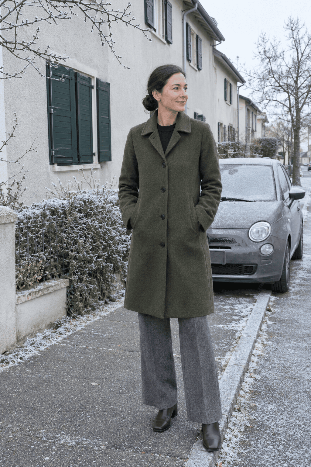 italian winter style for women: moss green knee-length wool coat, navy cashmere crewneck, mid grey wide straight trousers and dark brown block-heel ankle boots