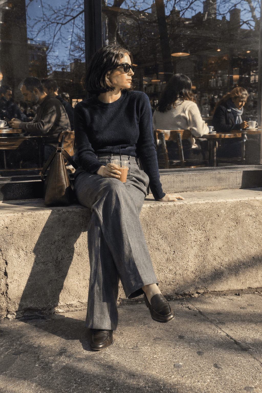 timeless capsule wardrobe office outfit: navy cashmere crewneck tucked into grey pleated wide-leg trousers with dark brown loafers