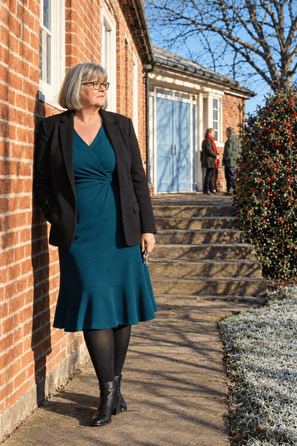 elegant plus size winter outfit for a woman in her 70s: deep teal V-neck dress with three-quarter sleeves, black ponte blazer and black block-heel ankle boots