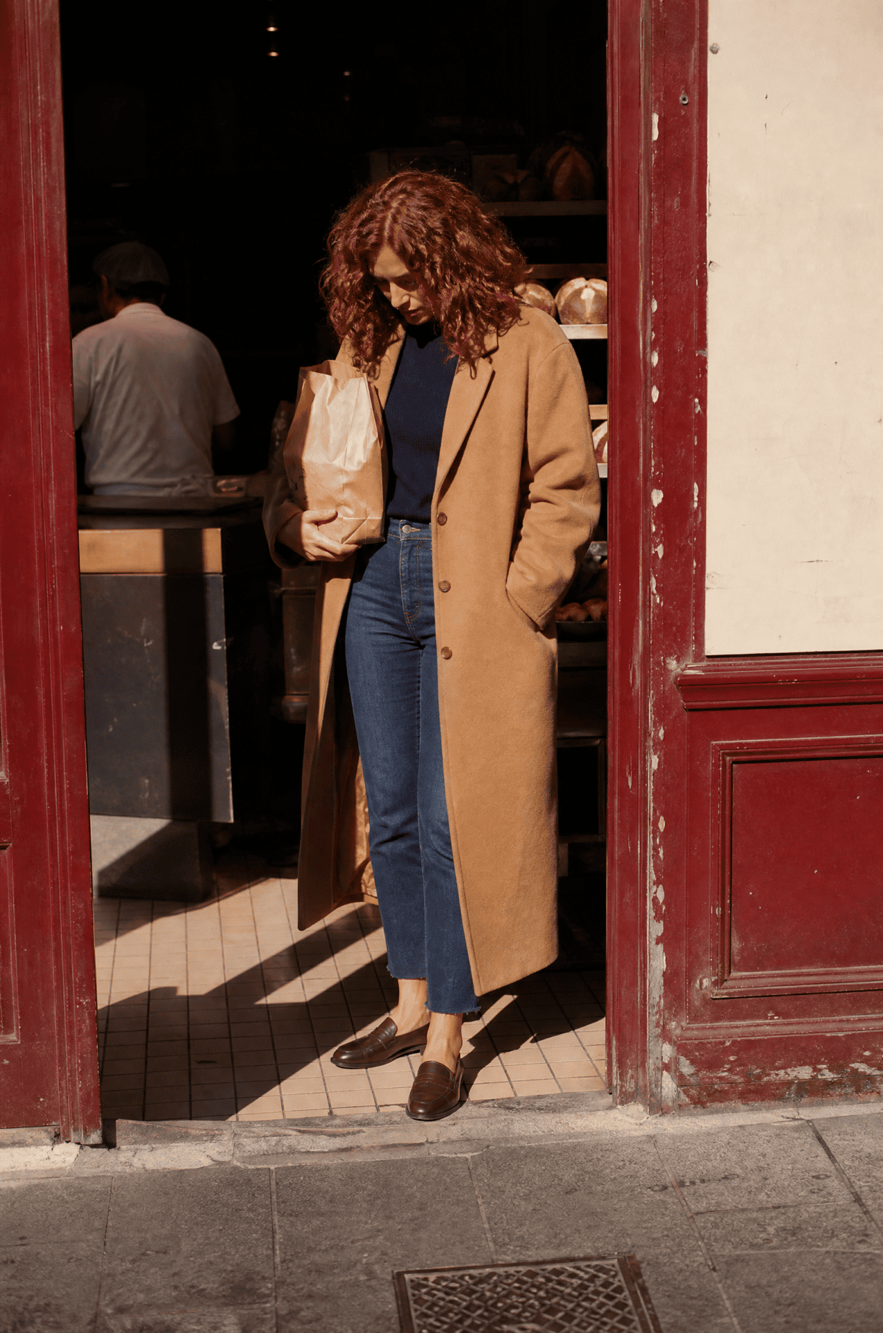 2027 capsule wardrobe errands outfit: camel topcoat, navy cashmere crewneck, dark indigo raw-hem jeans and dark brown loafers