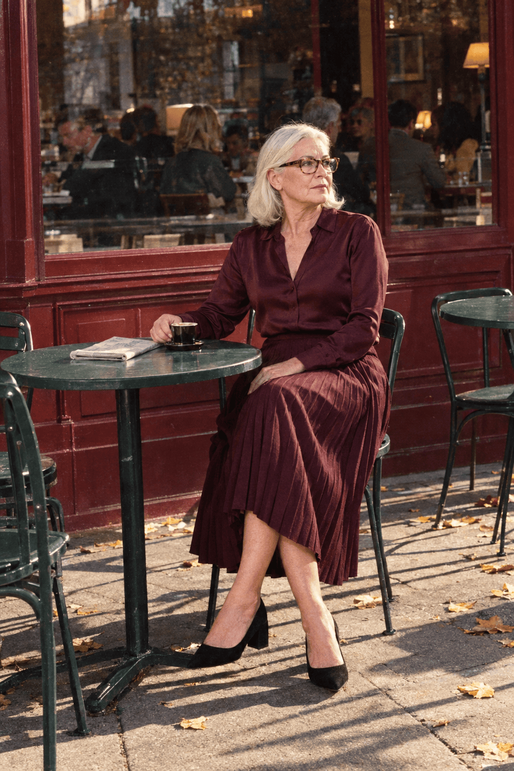 cocktail wedding guest outfit for a woman in her 70s: wine pleated midi skirt and matching wine long-sleeve silk blouse with black suede block-heel pumps