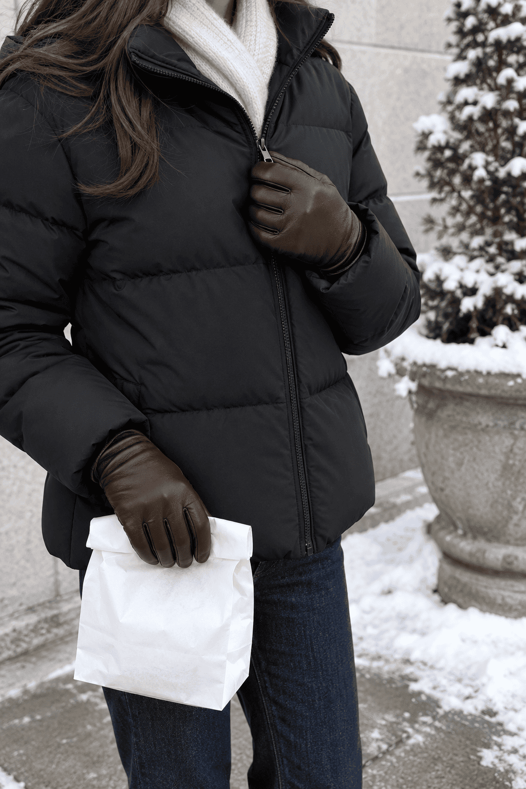 classy casual winter style: woman in plain dark brown leather gloves, a dark puffer coat and jeans on a winter errand