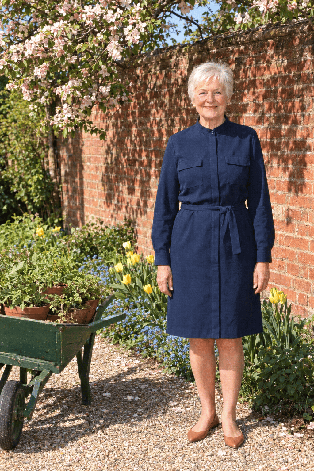 affordable spring outfit for a woman in her 70s: knee-length navy cotton stand-collar dress with long sleeves and tie belt, worn with tan leather ballet flats