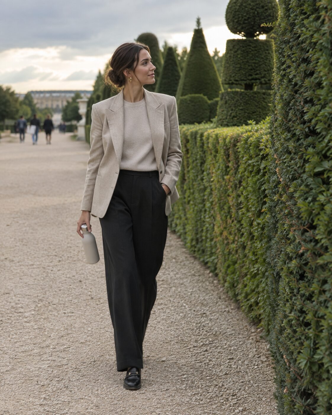 oatmeal linen blazer over a beige cashmere sweater with black wide-leg trousers and black loafers in a palace garden