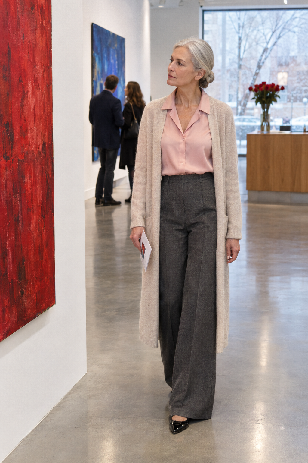 gallery date outfit for women over 60: vintage pink silk blouse tucked into charcoal wide-leg trousers with a long oatmeal cashmere duster and black pointed flats