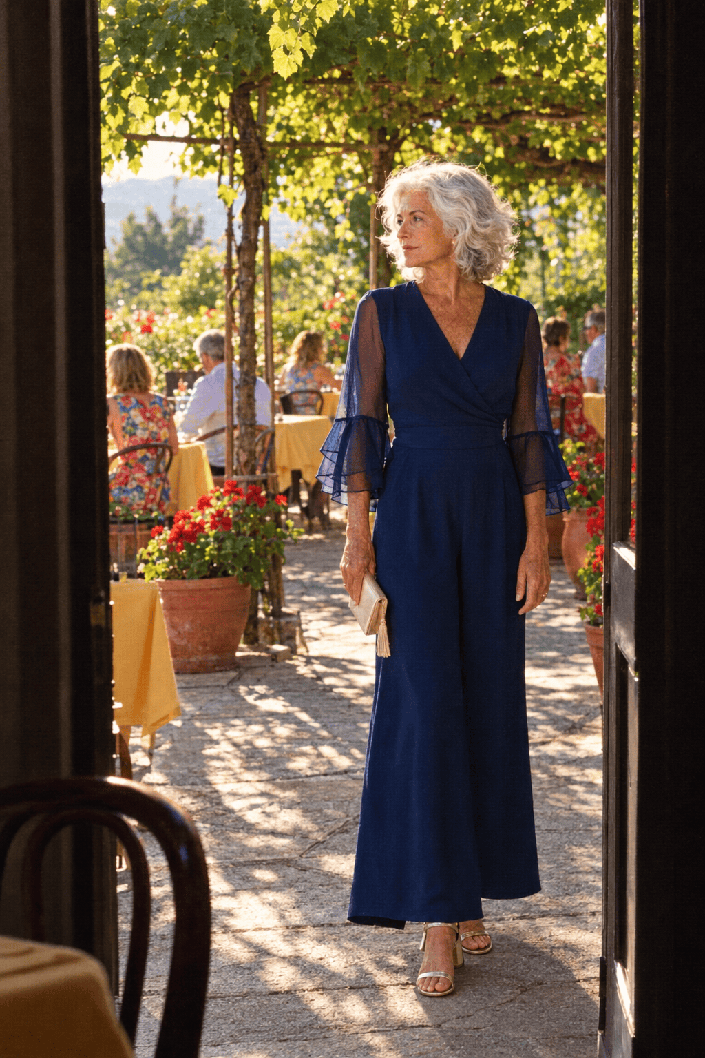 summer 70th birthday dinner outfit: navy crepe wide-leg jumpsuit with three-quarter sheer bell sleeves, soft gold low-heel sandals and champagne satin clutch