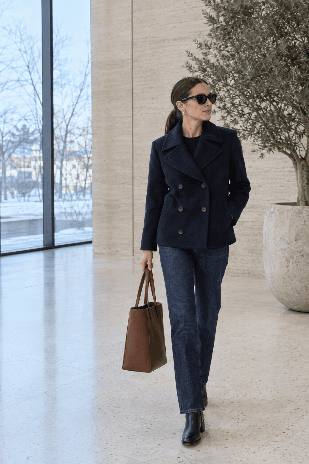 how to look elegant in winter: woman carrying a plain structured brown leather tote with a navy coat and jeans