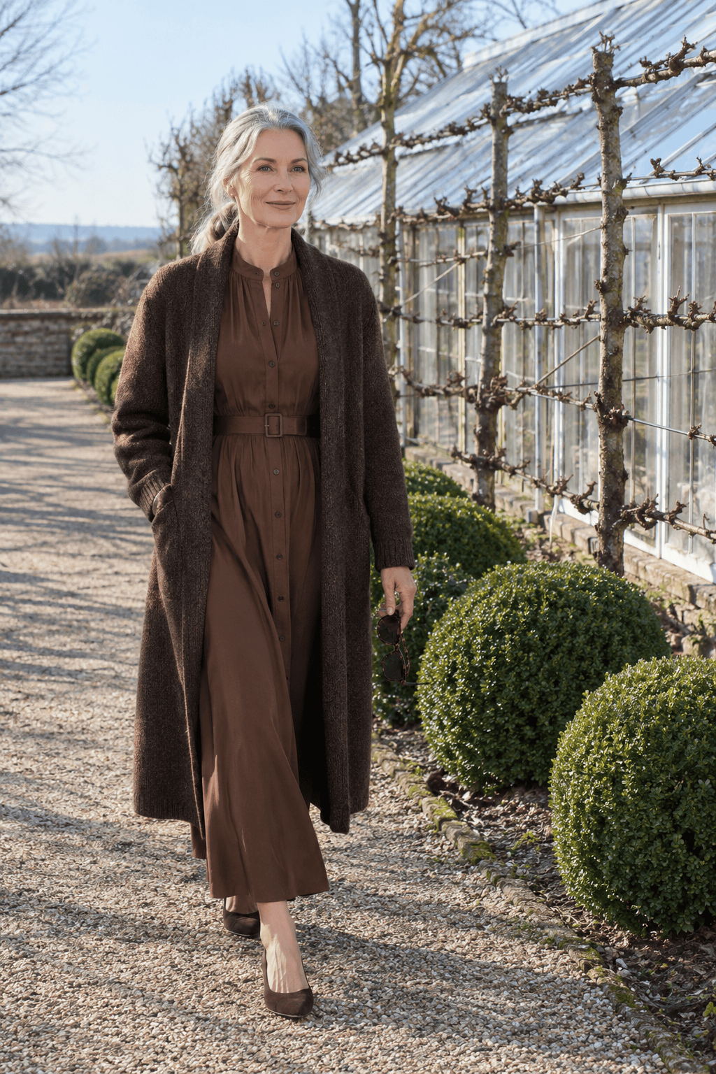 winter wedding guest outfit for women over 50: chestnut brown long-sleeve belted button-front dress, long chocolate coat and dark brown suede kitten-heel slingbacks