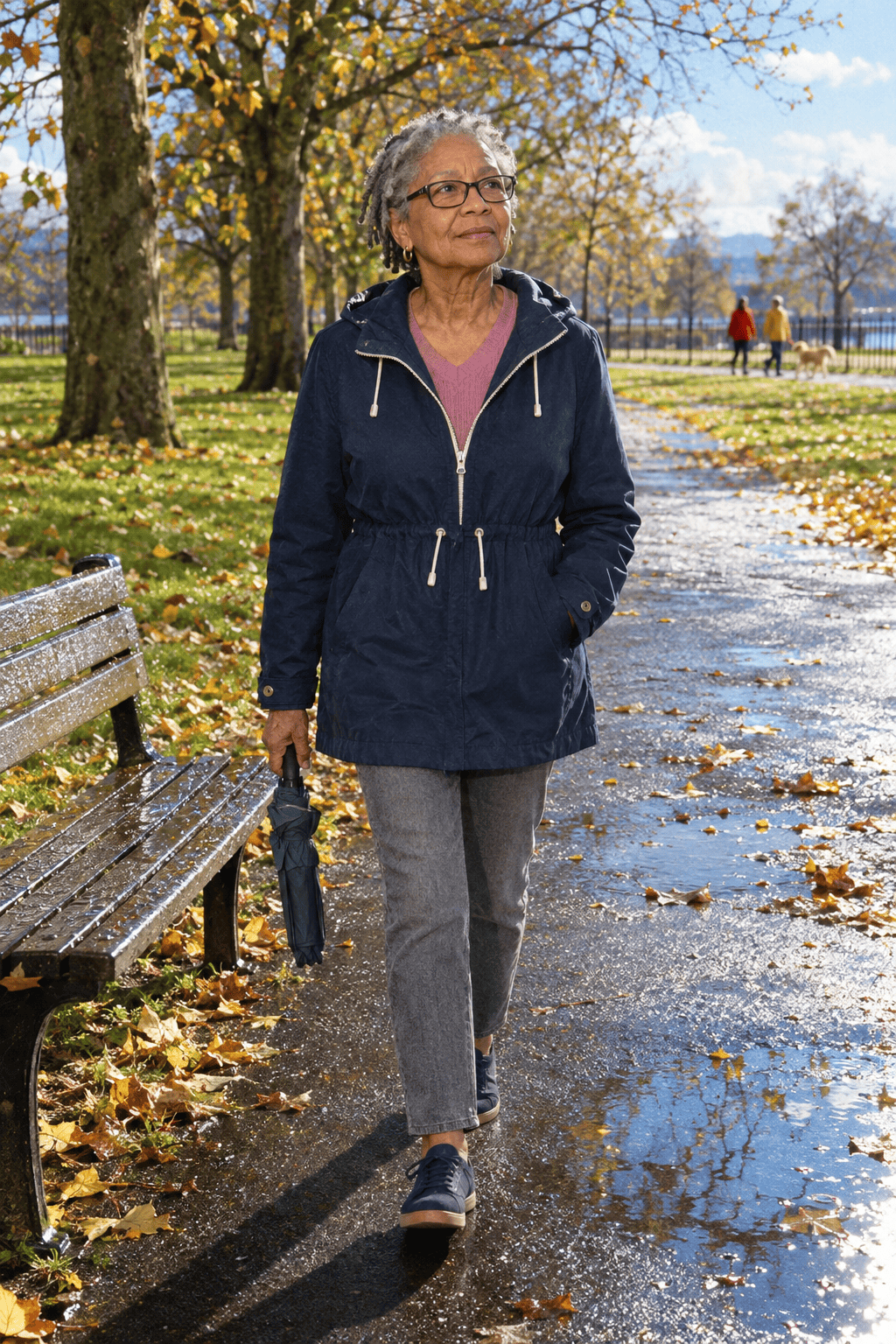 petite travel day outfit for a woman in her 70s: navy cotton anorak with a drawcord waist over a dusty pink V-neck sweater, gray ankle jeans and navy sneakers