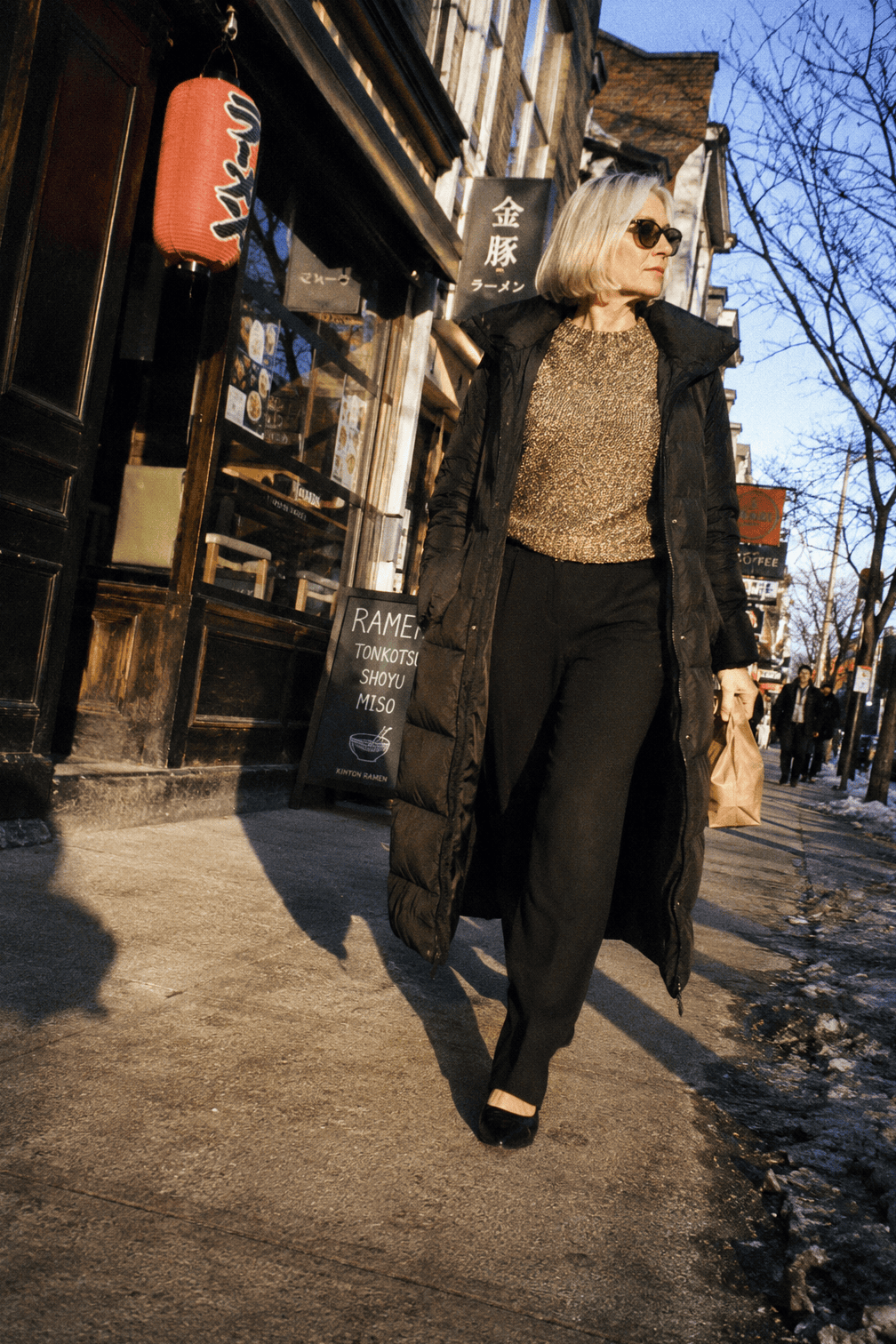 winter date night outfit: gold lurex knit sweater with black crepe trousers, pointed black leather flats and a long black down coat
