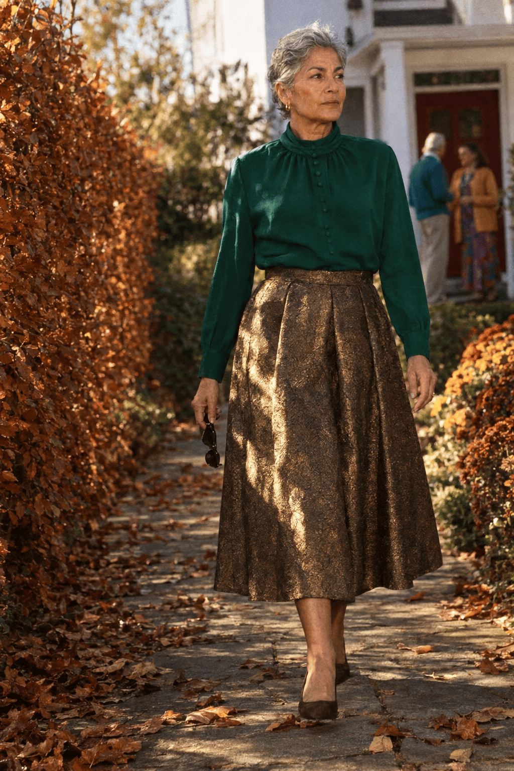 birthday dinner at home outfit for a woman in her 70s: bronze-gold metallic jacquard pleated midi skirt, emerald funnel-neck long-sleeve blouse and dark brown suede kitten-heel pumps