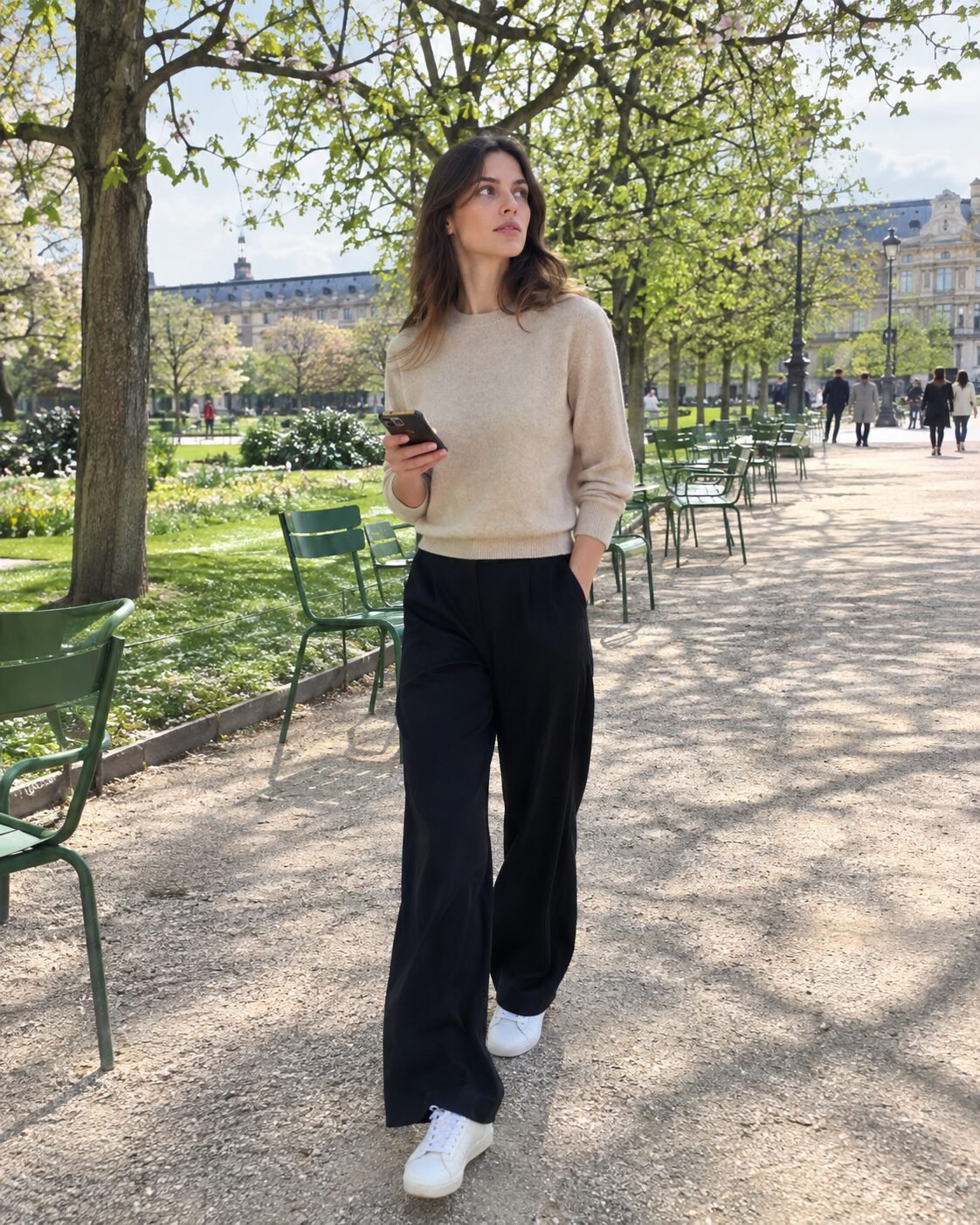beige cashmere sweater with black wide-leg trousers and white sneakers walking through the Tuileries garden