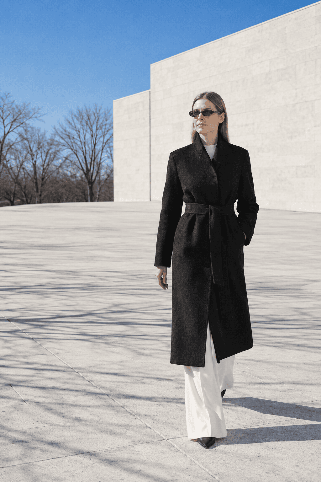 long black coat outfit with wide-leg trousers: belted black wool coat over an ivory cashmere crewneck and ivory pleated wide-leg trousers on a bright winter day