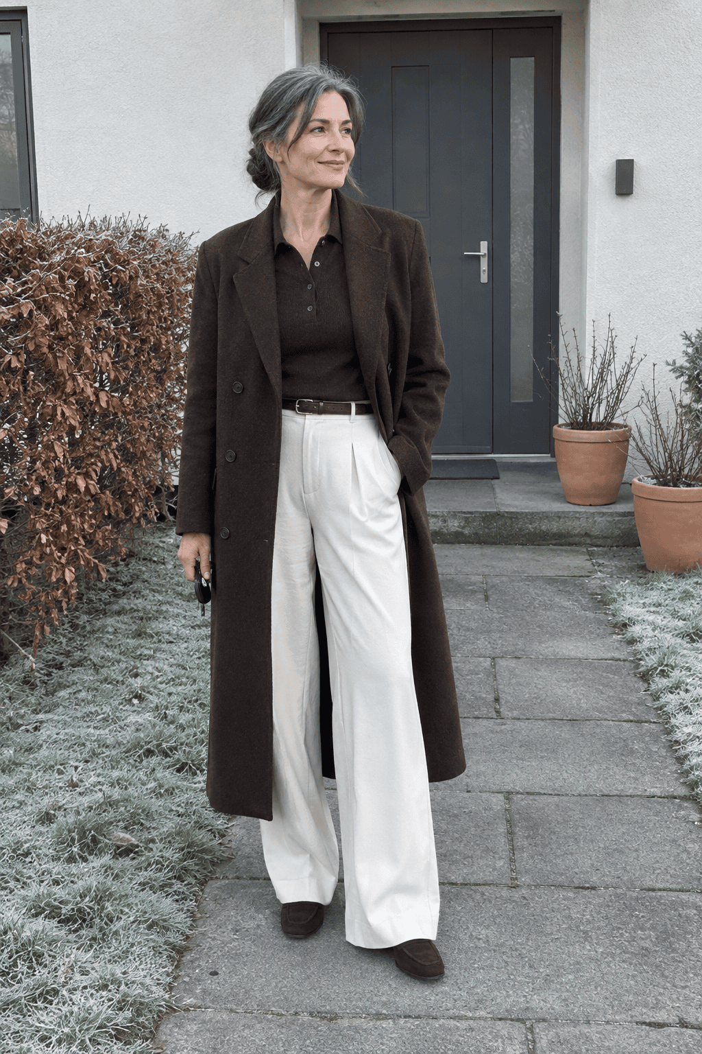 elegant winter outfit for women over 50: long chocolate wool coat over a chocolate cashmere polo sweater, cream wide-leg trousers and chocolate suede loafers