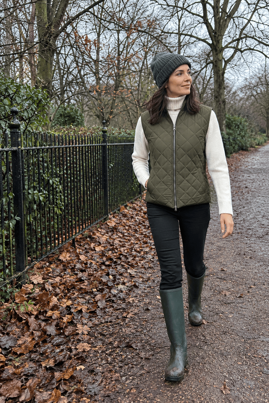 what to wear in London in winter for a park walk: olive quilted gilet, ivory cashmere roll neck, black trousers and dark green tall rain boots