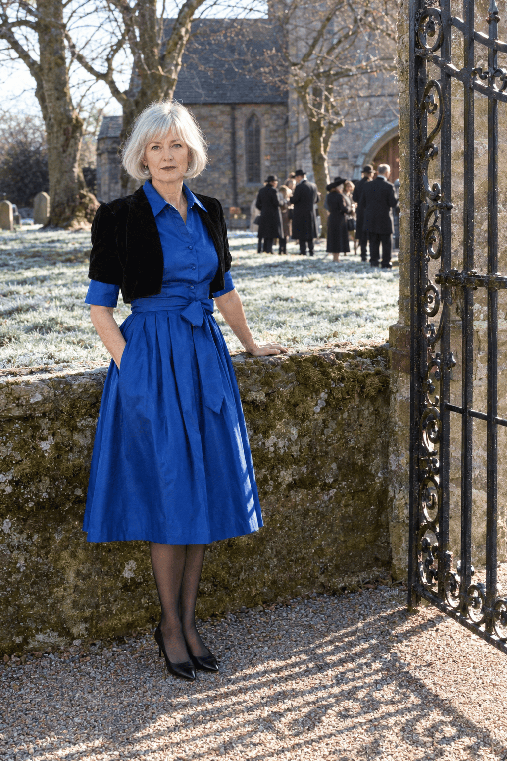 church wedding mother of the groom winter outfit: knee-length sapphire taffeta shirt dress with elbow sleeves and a sash, a cropped black velvet bolero and black kitten heels
