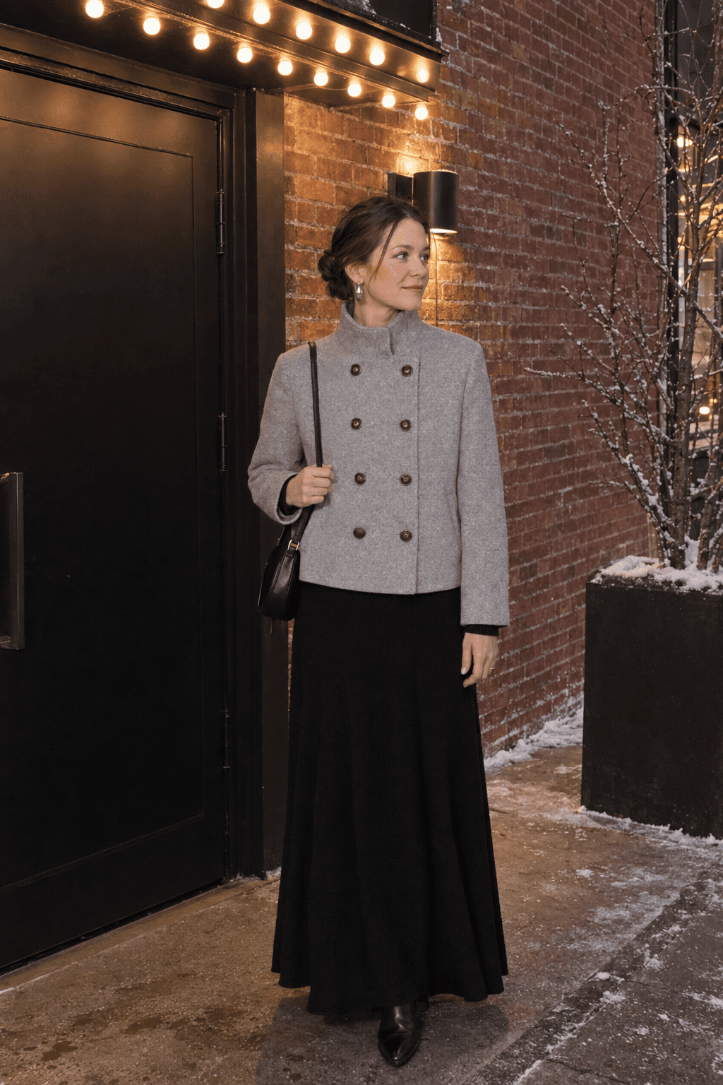 new years eve theatre outfit: long-sleeve black knit fit-and-flare maxi dress with a light grey double-breasted wool coat and chunky silver hoop earrings