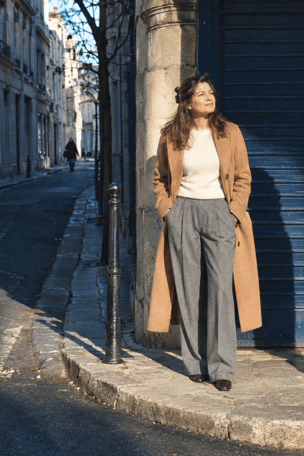 capsule wardrobe city day outfit: camel topcoat, ivory cashmere crewneck, grey pleated wide-leg trousers and dark brown loafers