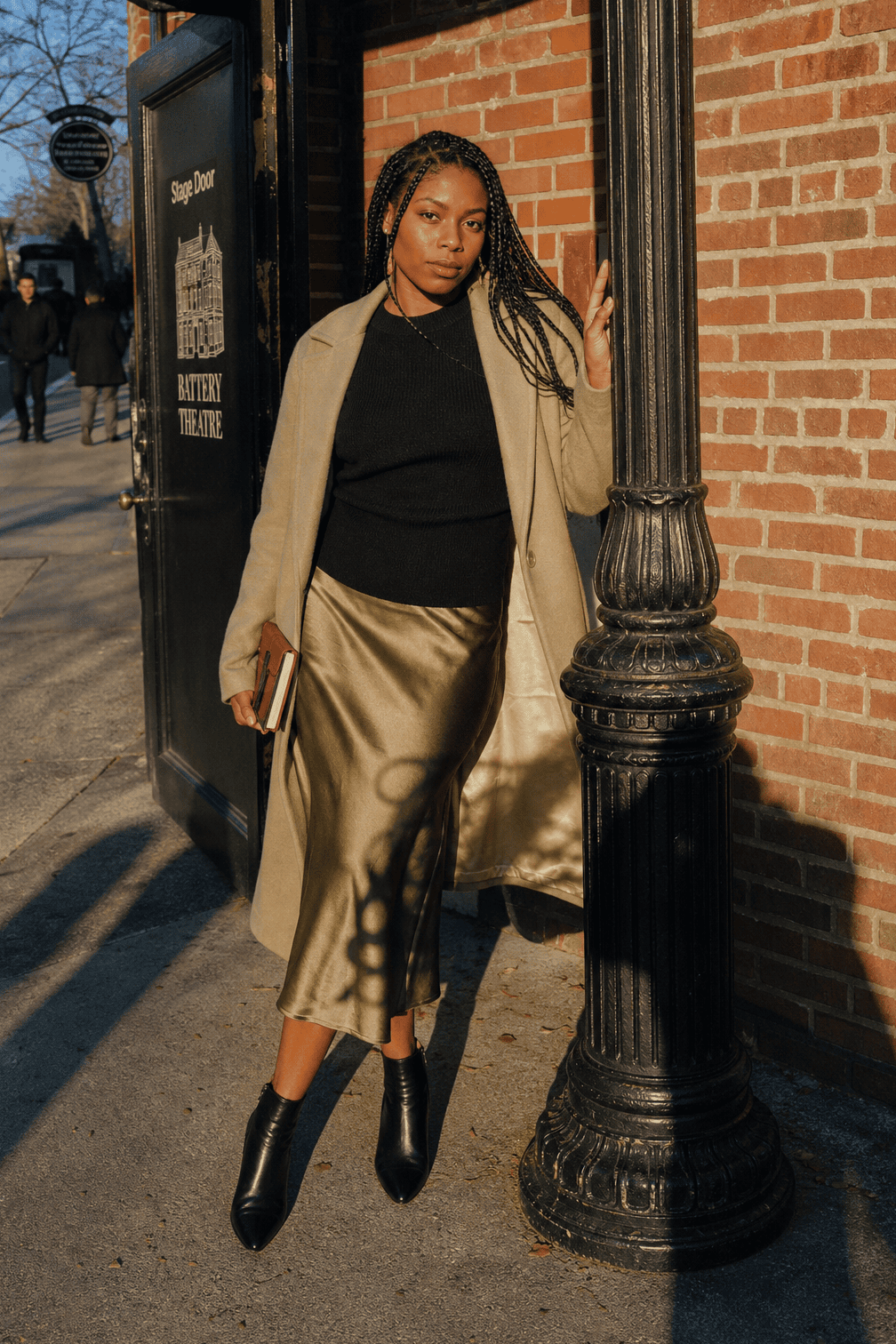winter date night outfit: black cashmere crew sweater with an olive satin midi skirt, black leather ankle booties and a belted wheat wool blanket coat