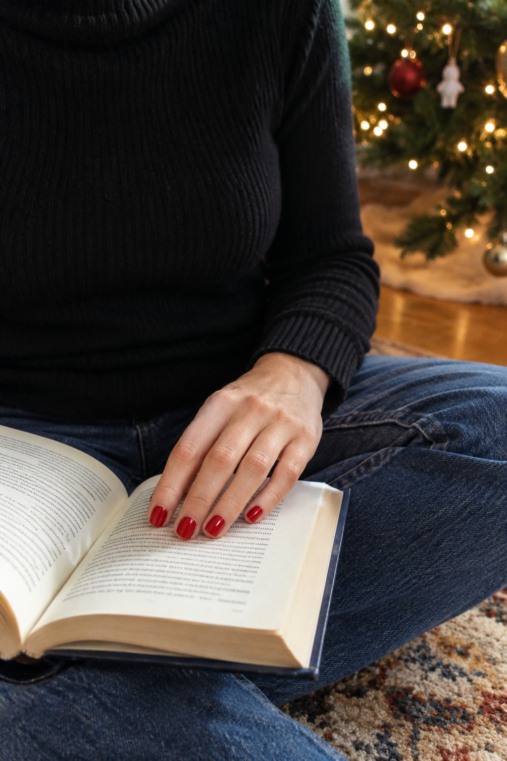 classy christmas nails in a blue-based true red cream polish resting on an open book by the christmas tree