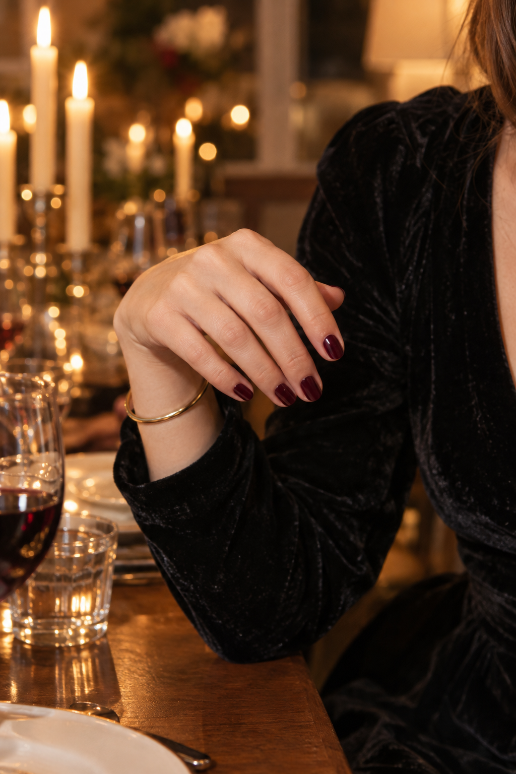 elegant holiday nail colors: bordeaux wine polish on short nails with a gold bangle at a candlelit christmas eve table